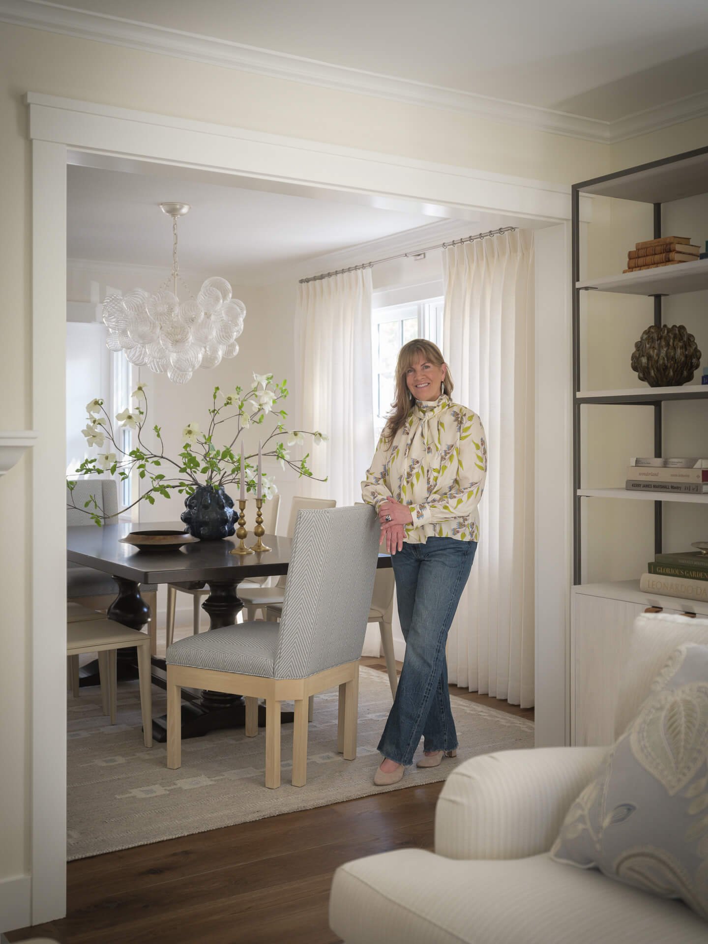 Leaf Ives standing in a light-filled dining room with pale furnishings and a chandelier.