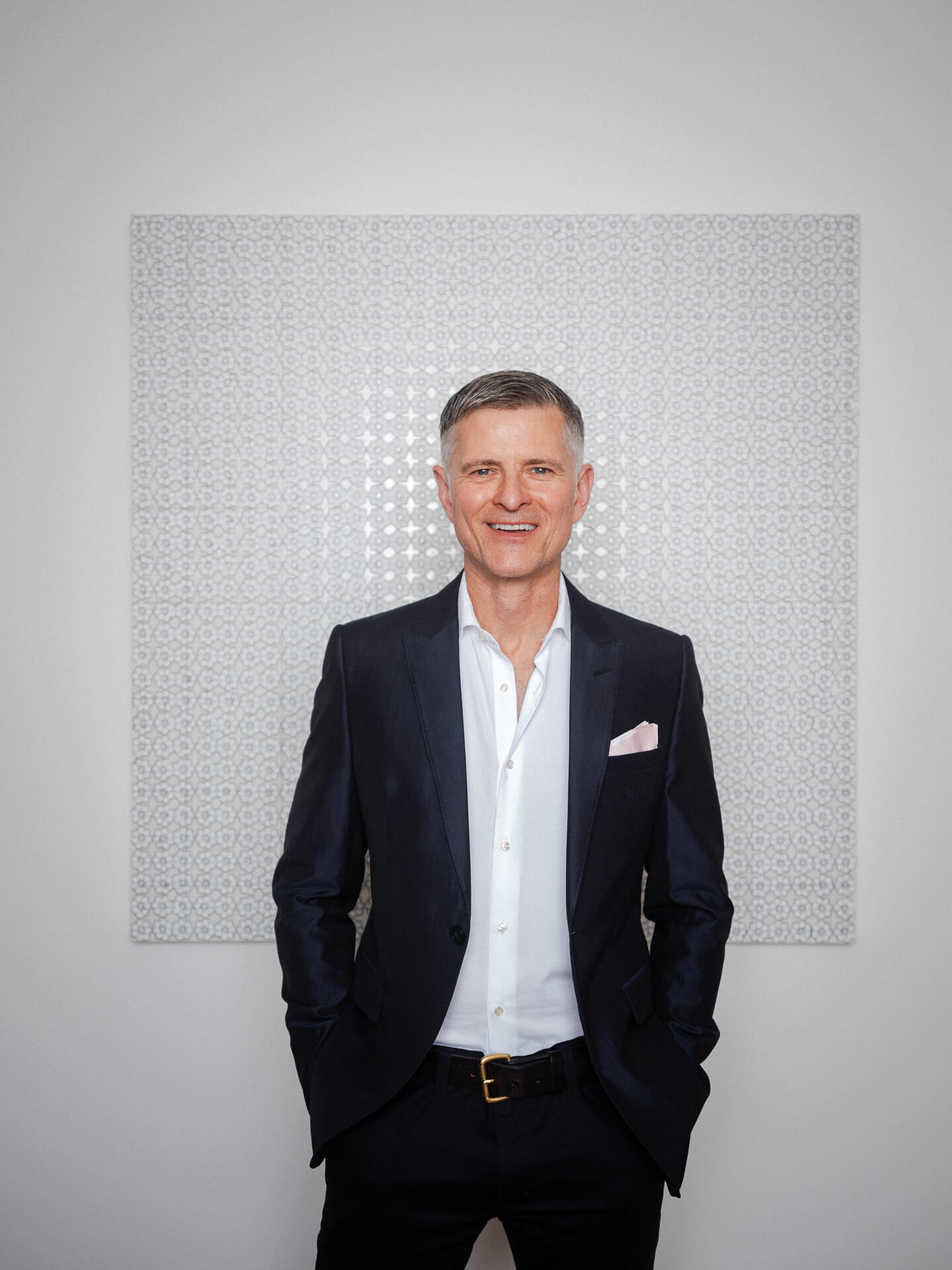 Michael Miller standing in a dark suit against a pale textured artwork.