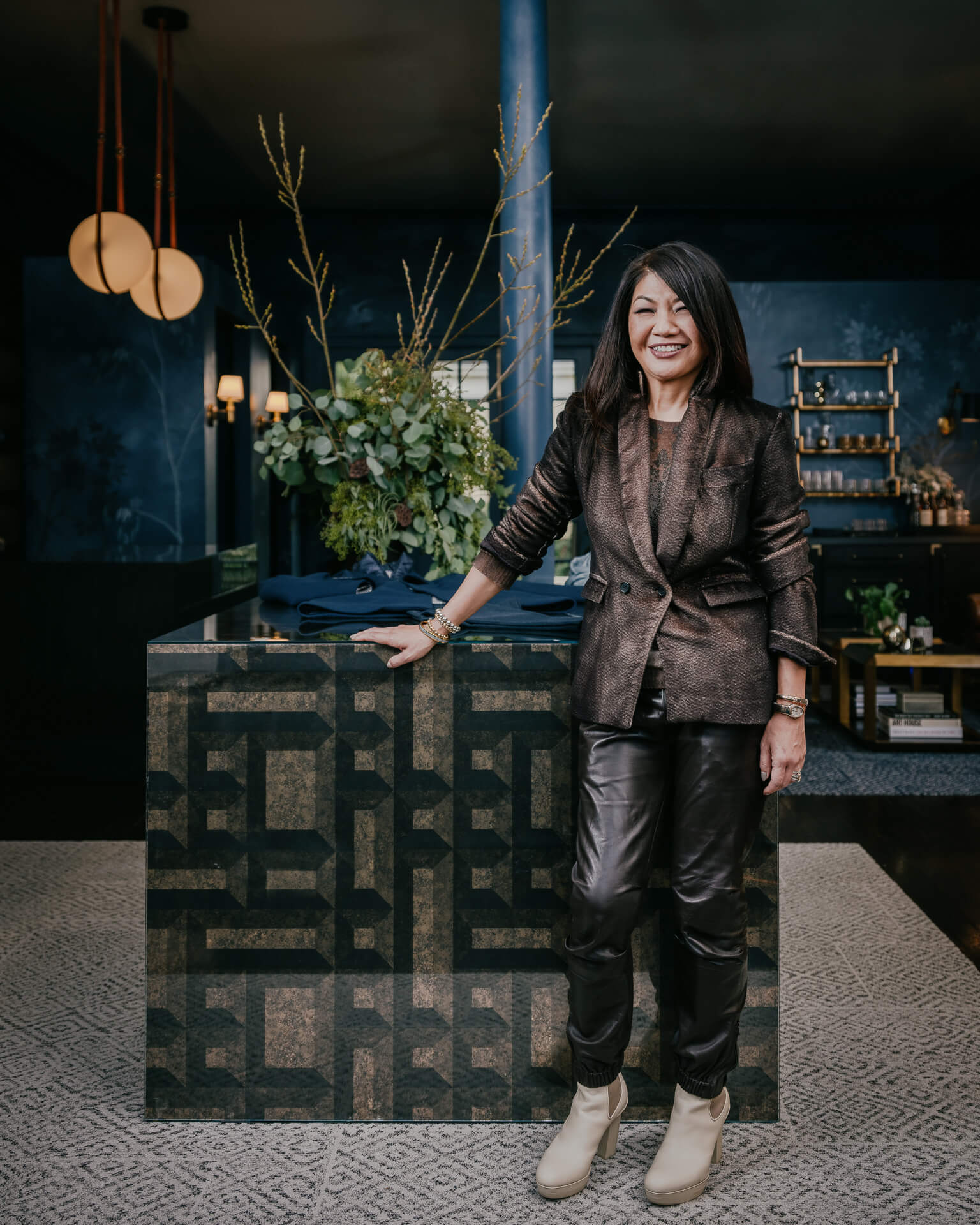 Mr. Lin owner standing in a dramatic dark interior with patterned tile, flowers and sculptural lighting.