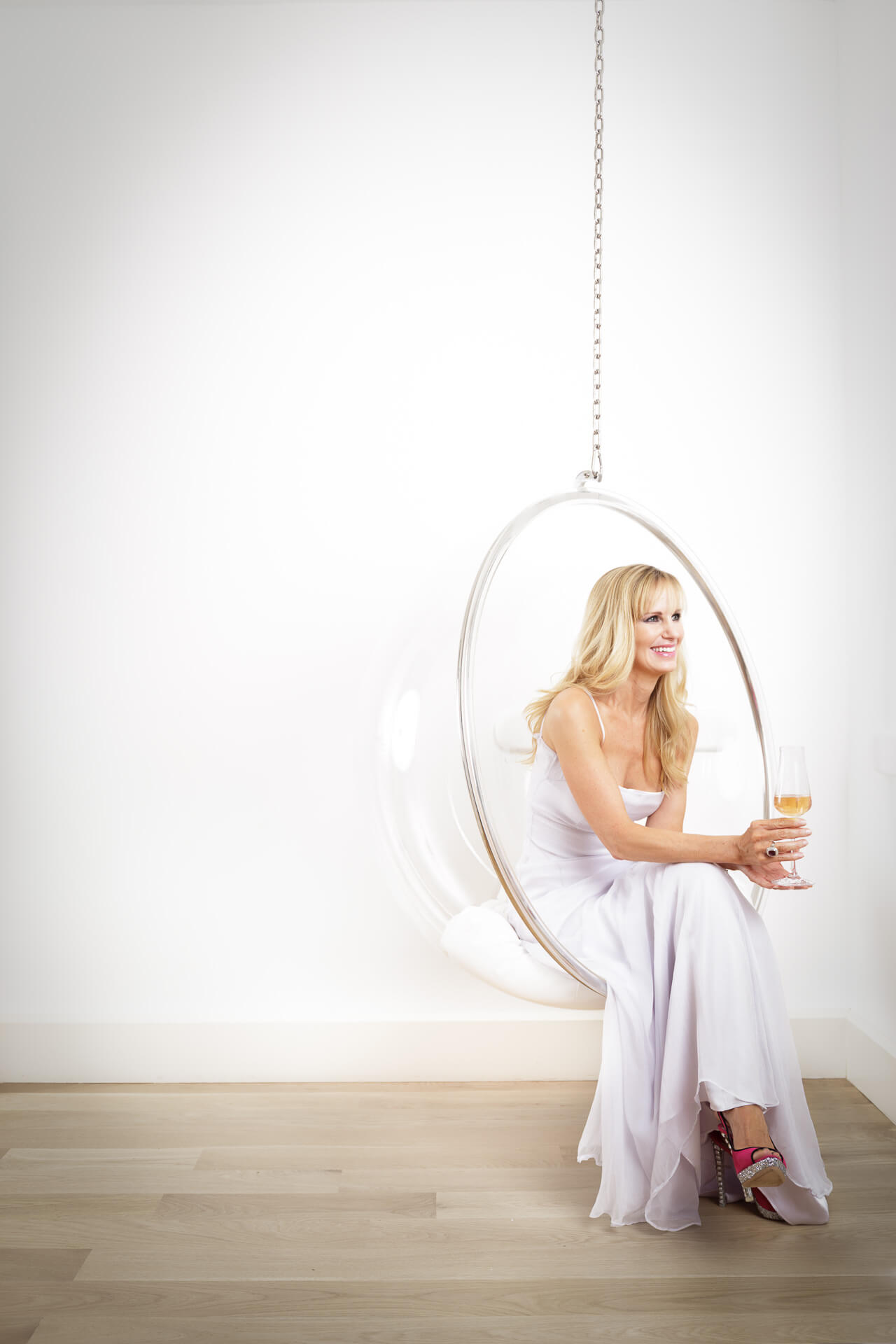 Sherri Corker seated in a transparent hanging chair against a bright white interior.