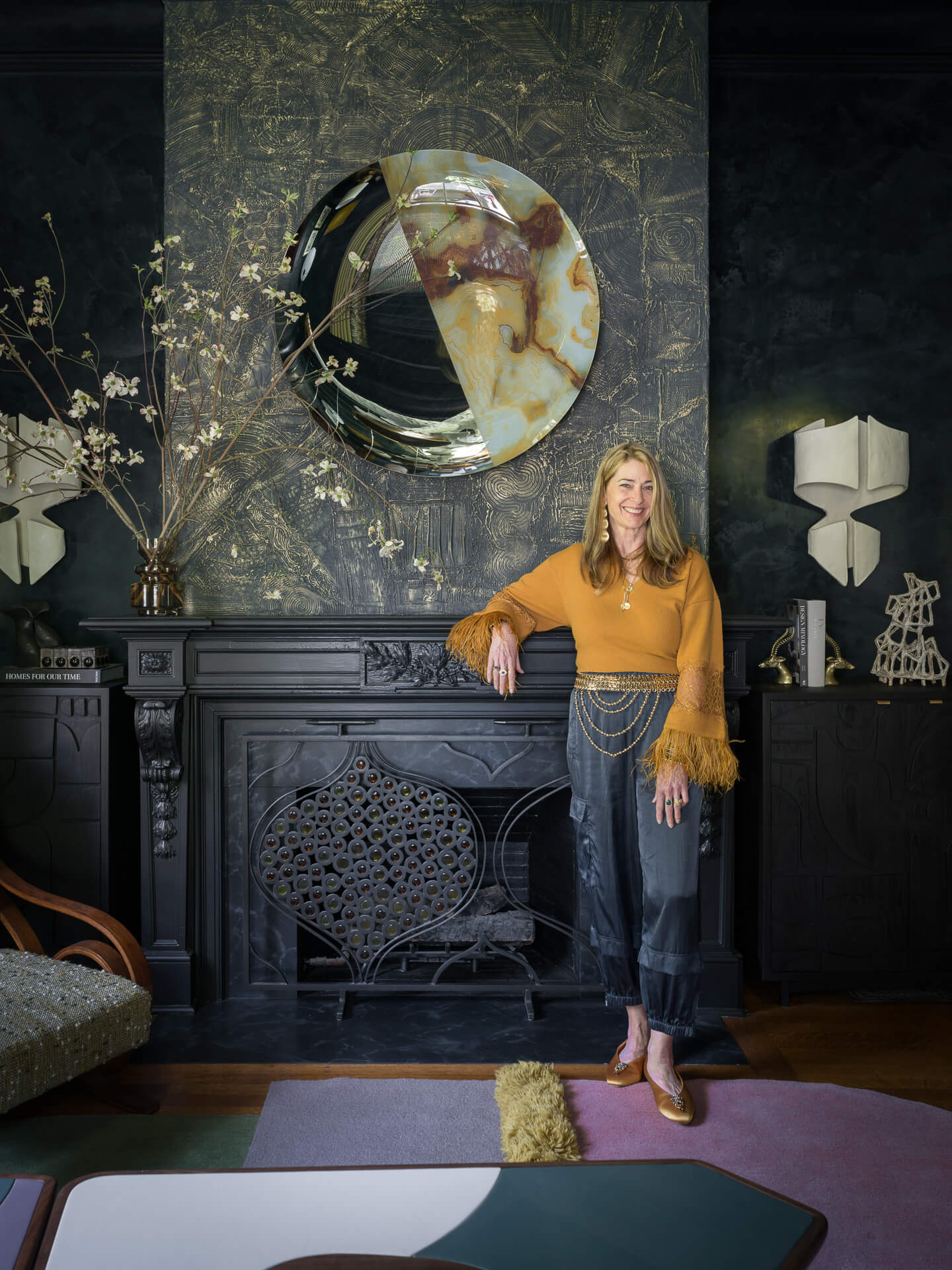 Tineke Triggs standing beside a dark fireplace beneath a circular artwork in a dramatic interior