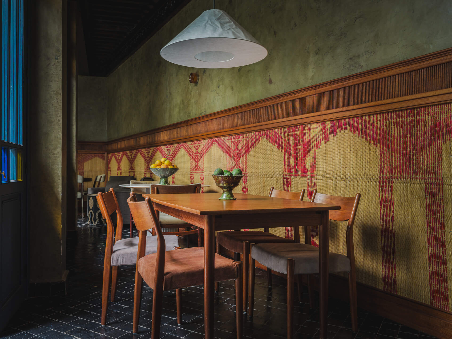 Moody dining room with wood table and chairs against patterned red-and-natural woven wall panels.