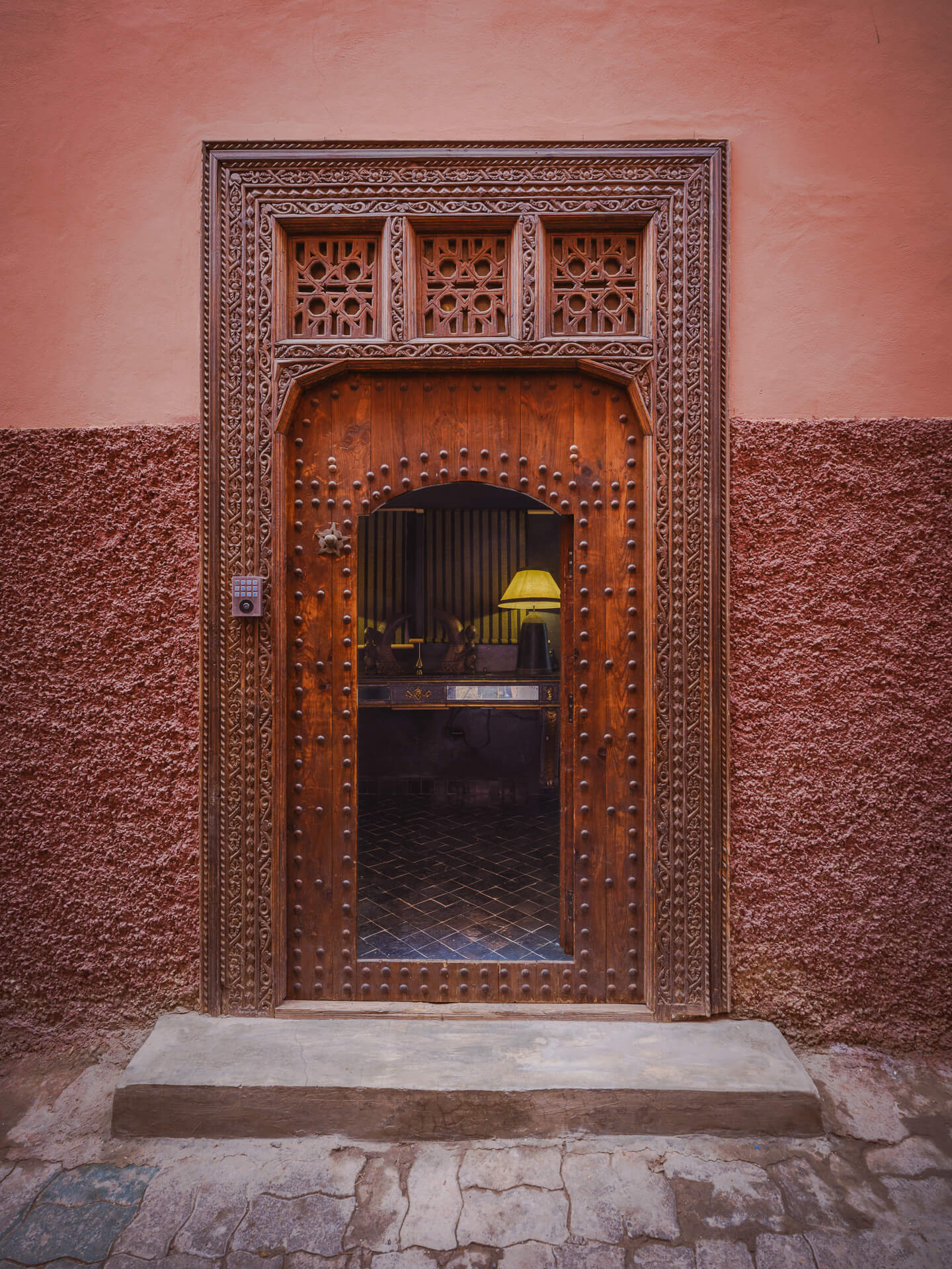 Ornately carved wood doorway set into textured pink plaster walls.