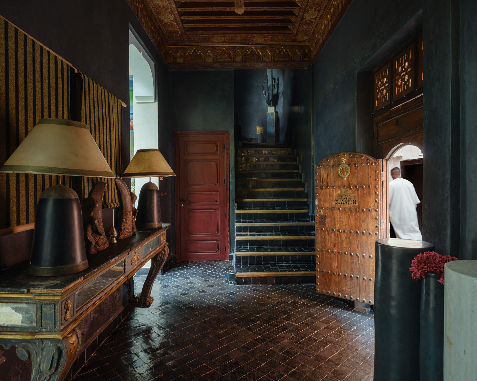 Dramatic entry hall with dark tiled floor, carved wood ceiling, and stairs leading upward.