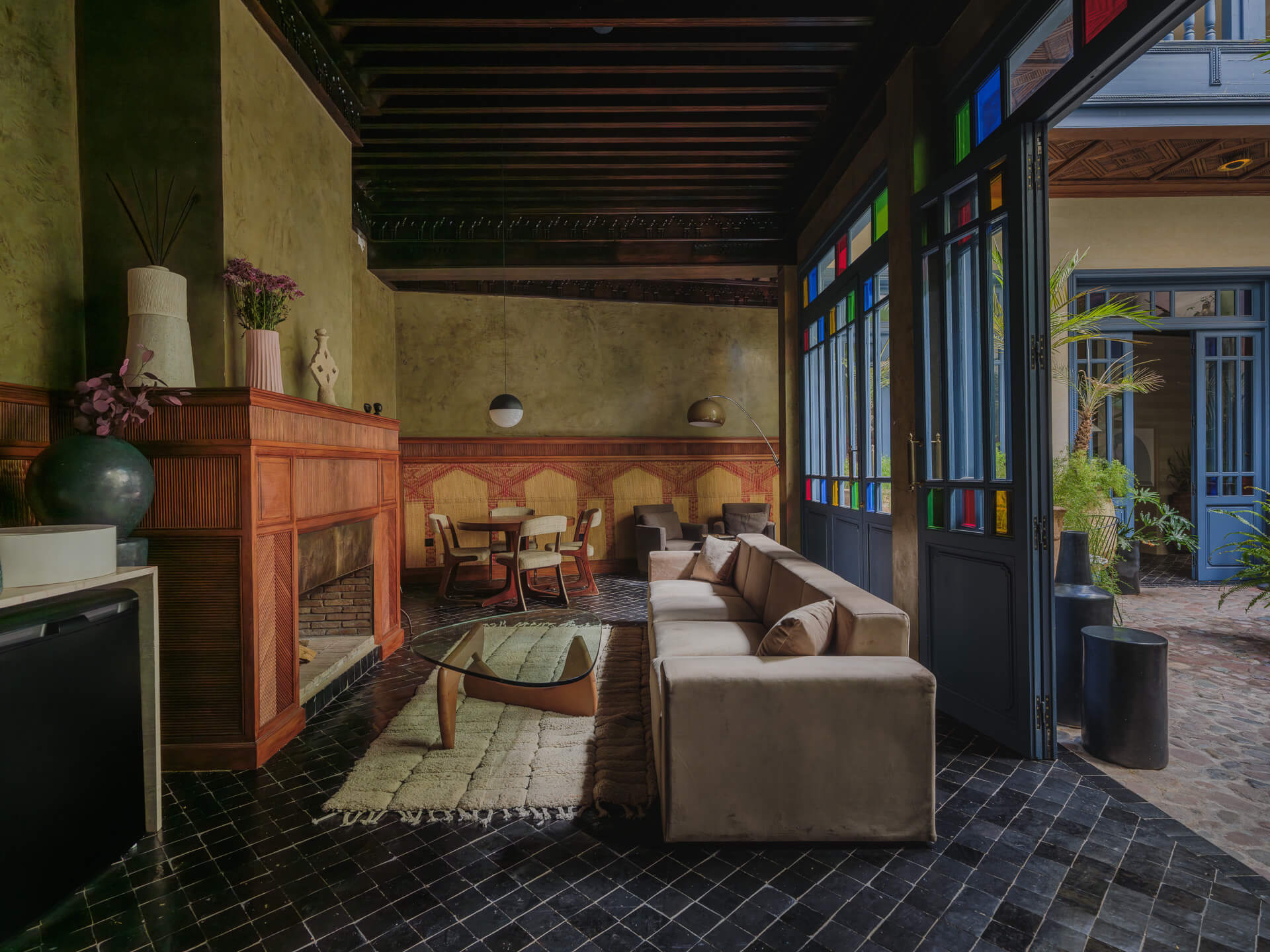 Living room with fireplace, neutral seating, dark tiled floor, and colorful glass doors opening to the courtyard.