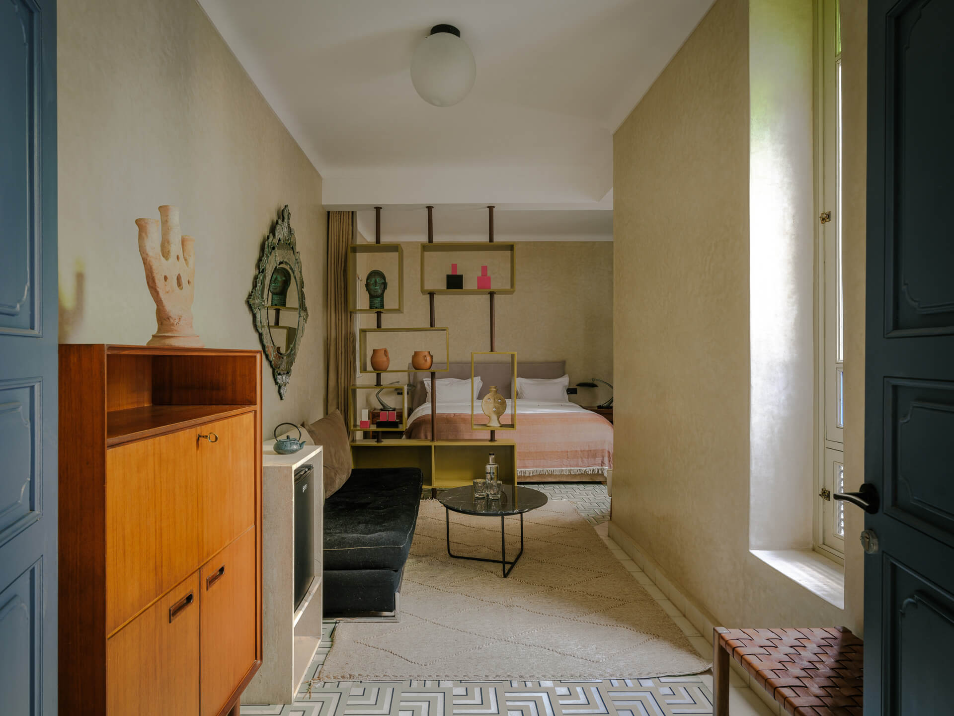 Bright sitting room with wood cabinetry, pale seating, open shelving, and patterned tile floor.