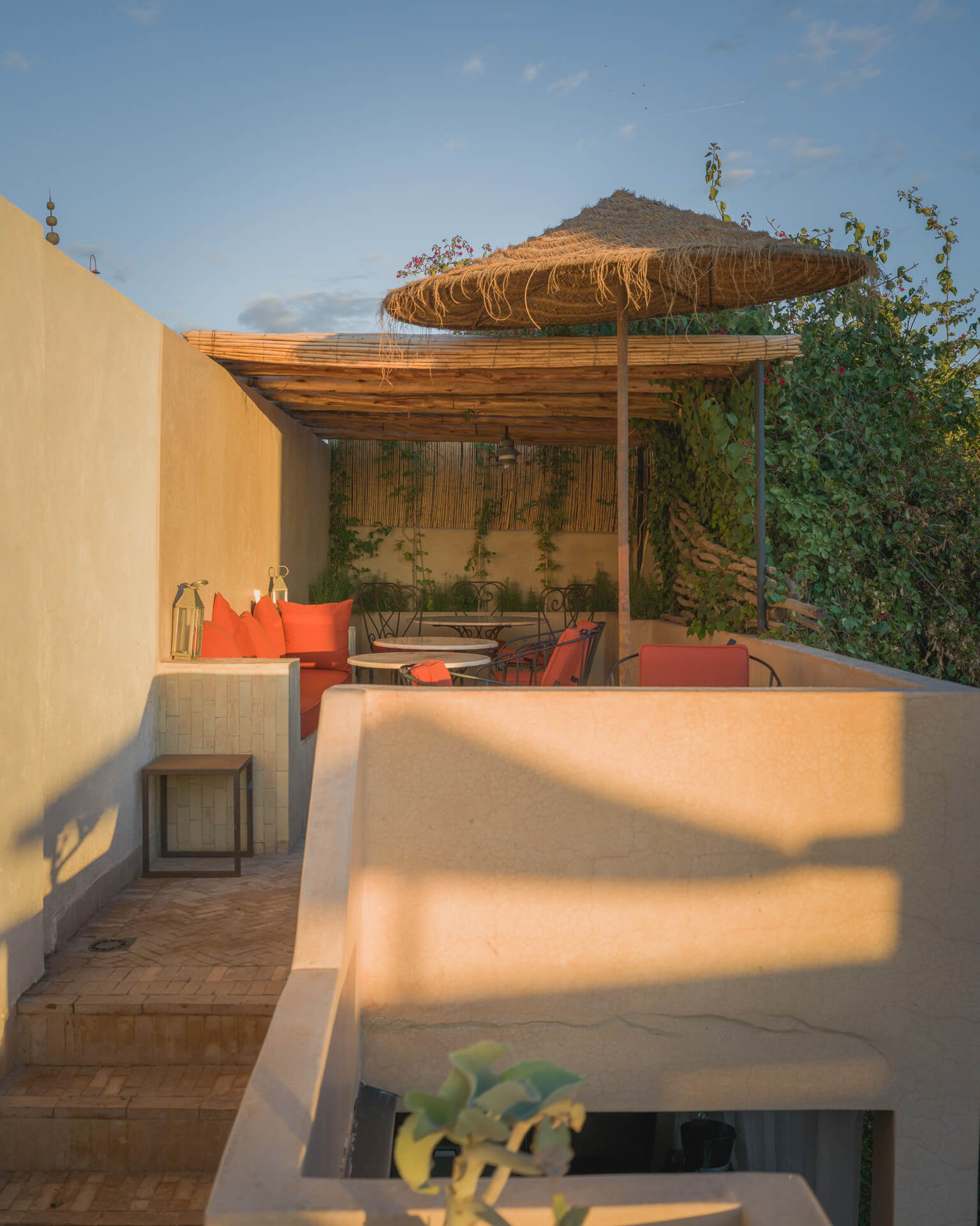 Rooftop lounge with red cushions beneath a woven canopy in warm late-day sunlight.