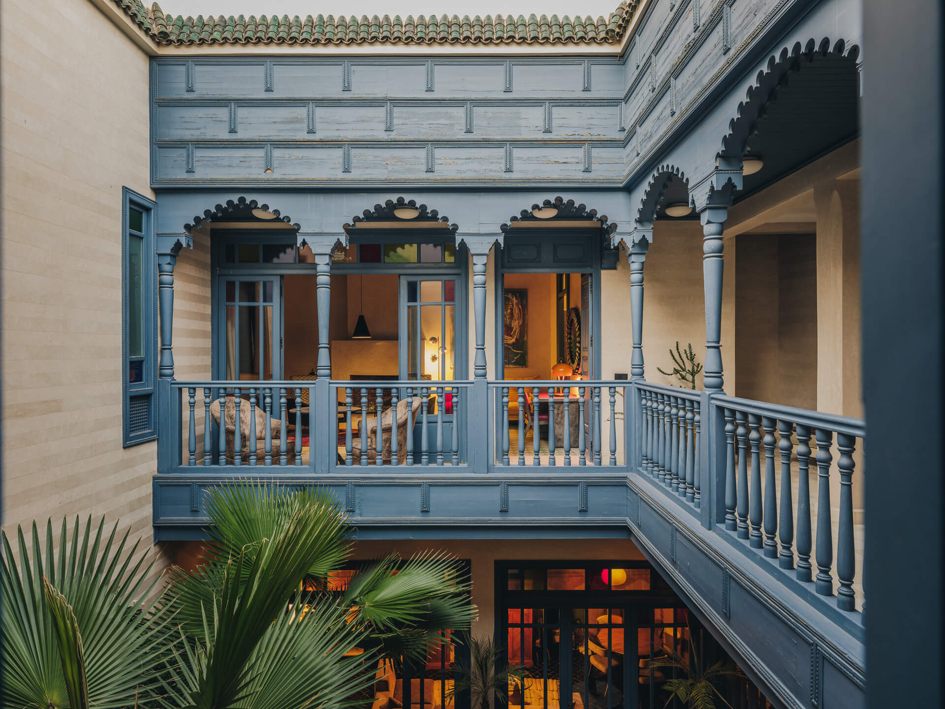 Interior courtyard framed by blue-painted balconies, carved arches, and lush palm foliage.