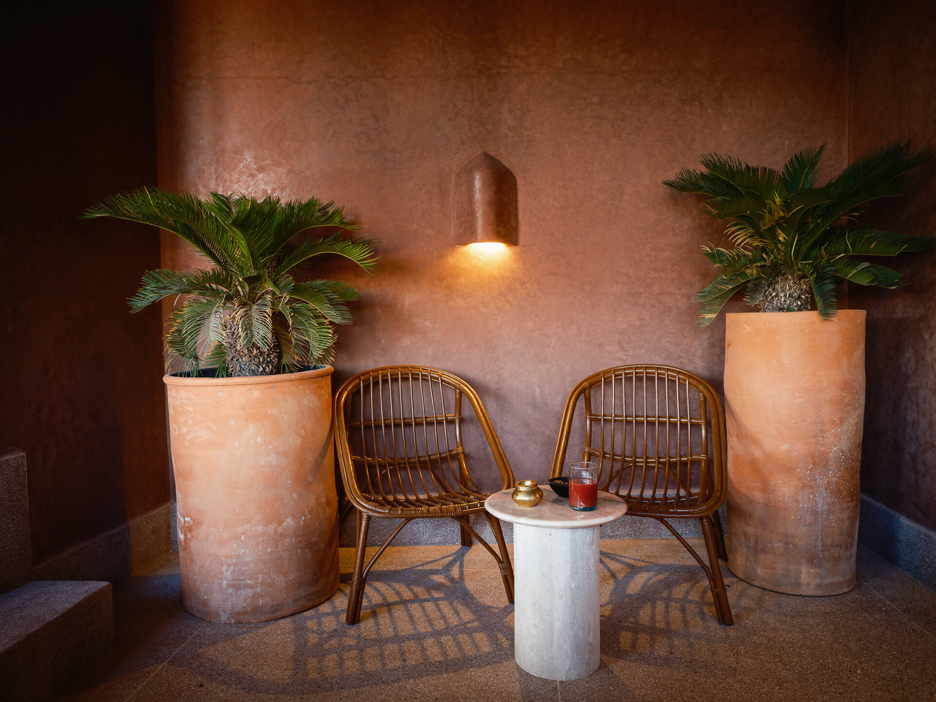 Intimate seating nook with two wicker chairs, large potted palms, and a small round table.