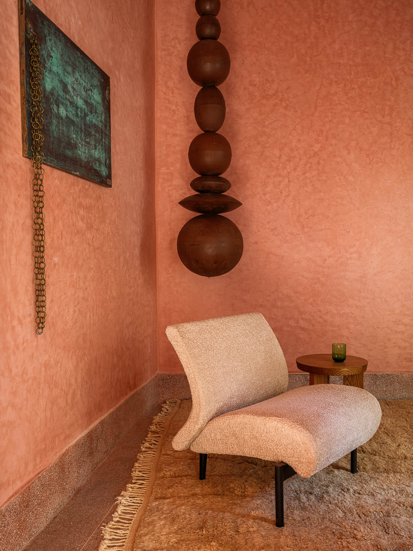 Upholstered lounge chair beneath a hanging wood sculpture against a textured red plaster wall.