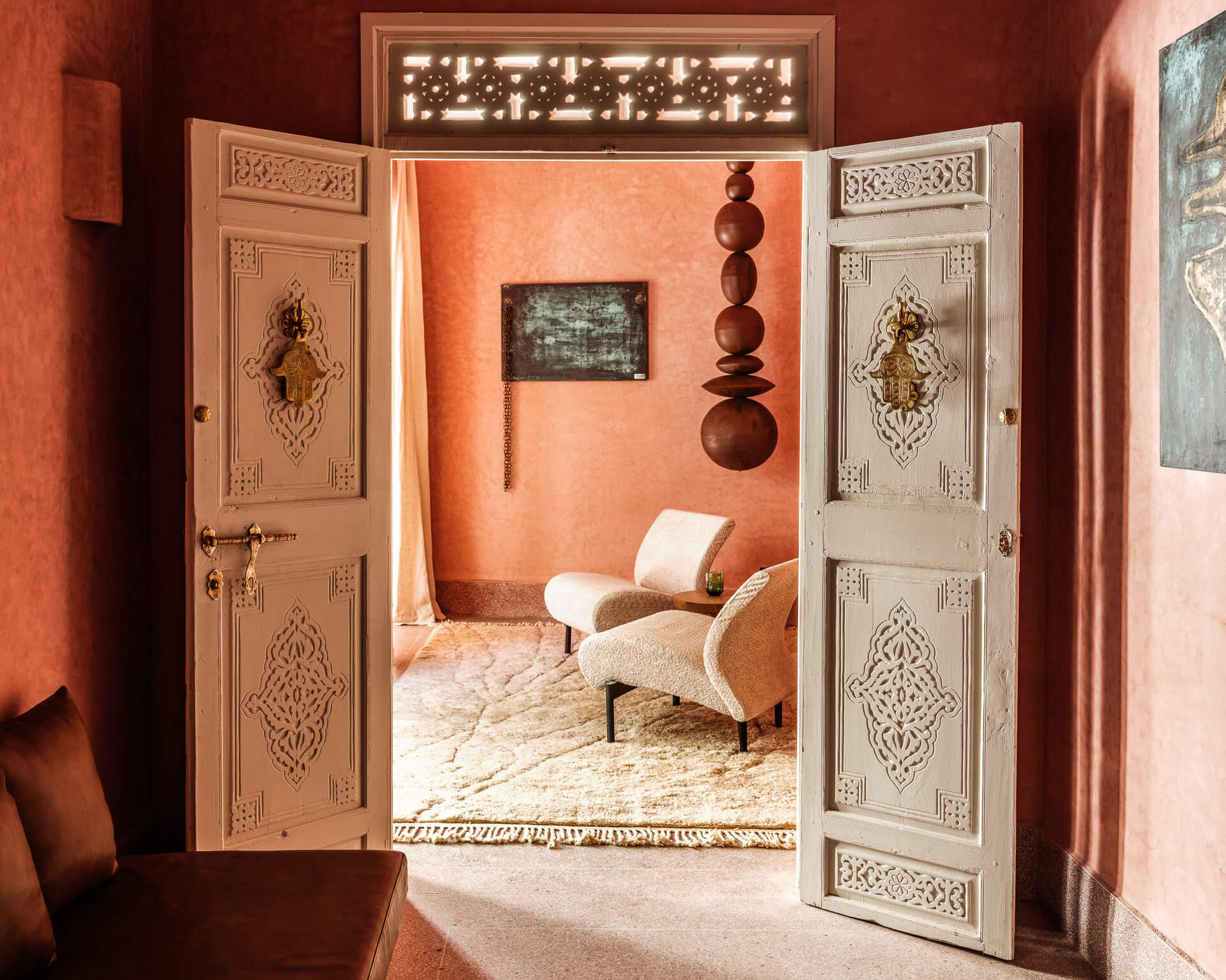 Ornate white double doors opening into a red-walled sitting room with a pale lounge chair.