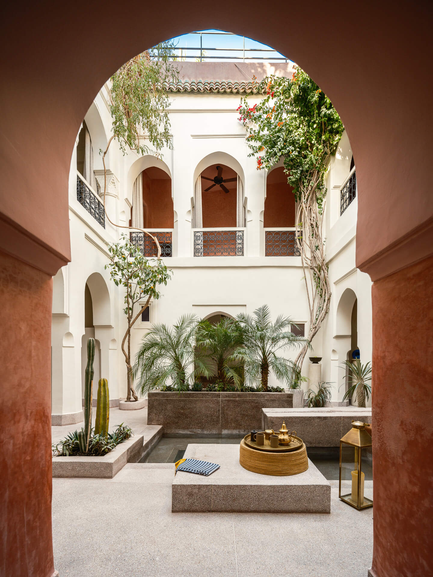 Large red plaster arch framing a white courtyard with balconies, greenery, and sculptural furnishings.