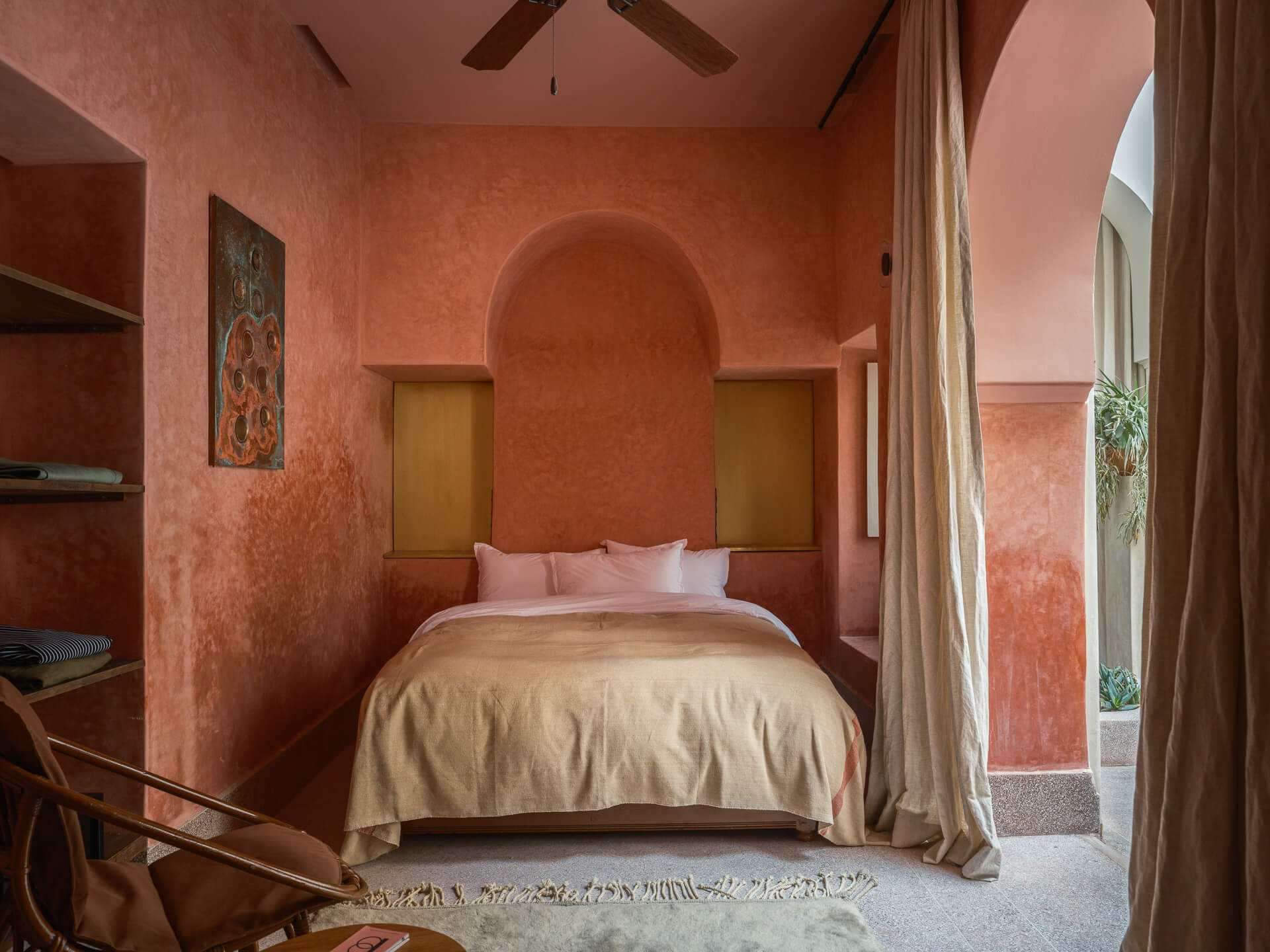 Cozy bedroom with red plaster walls, exposed wood beams, and a bed set into a rounded alcove.