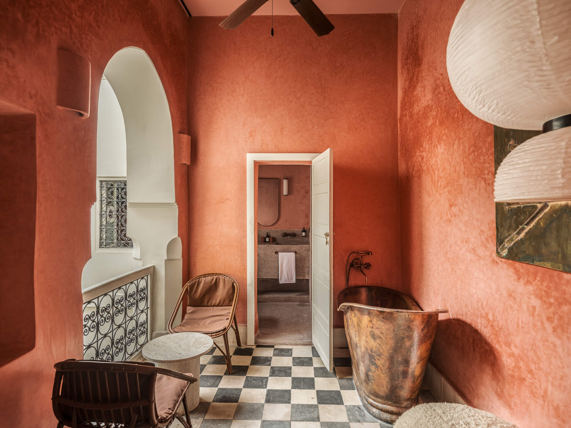 Red plaster bathroom with black-and-white checkerboard floor, freestanding copper tub, and arched doorway.